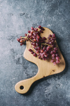 Wooden serving board with fresh red grapes over blue texture background. Top view, copy space. Toned image