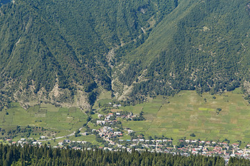 Fototapeta na wymiar a view from a height to a small mountain village at the foot of the wooded mountains, surrounded by a delimited agricultural land