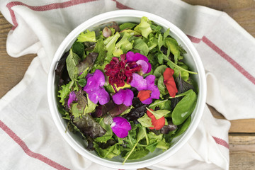 High angle view of mixed salad with eatable flowers in bowl standing on dishcloth