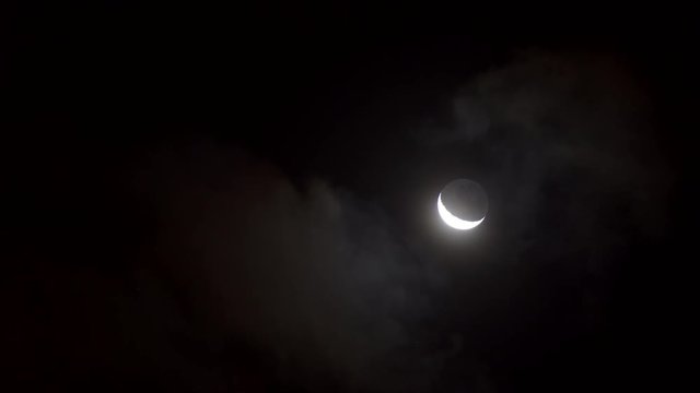 Young moon mooving through clouds at night