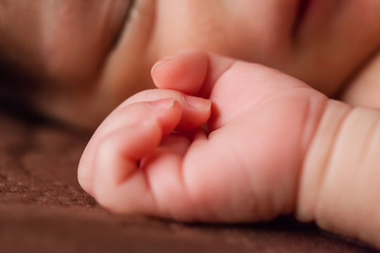 Close up of a tiny and delicate hand of a cute small two weeks old newborn baby girl, sleeping peacefully in bed