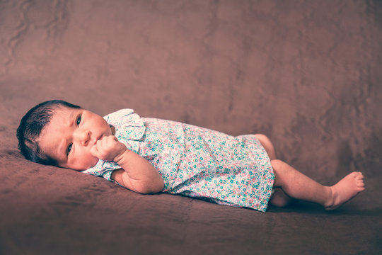 Cute two weeks old newborn baby girl lying down, eyes open and looking around wearing a floral dress