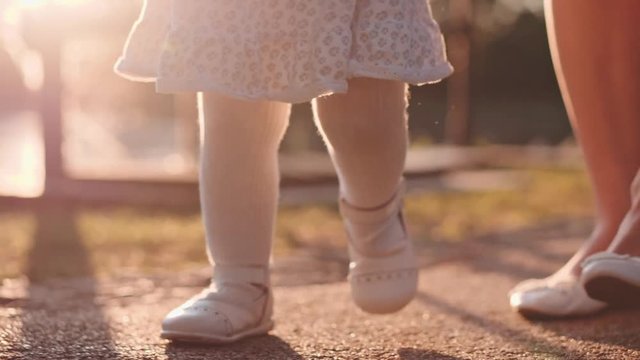 Little baby learns to walk. First Steps. Slow Motion 120 fps, 4K. Mother is teaching her child to do the first steps on a park road in summer. Close up on feet. Happy childhood and Maternity. Family