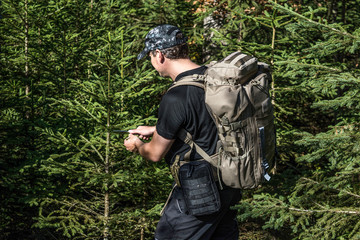 Man with tactical backpack with MOLLE system in woods.