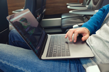 Young man in jeans uses laptop for writing software code in transport. Close up.
