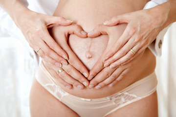 hands of the father and mother make a heart on the pregnant tummy