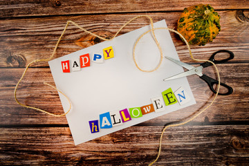 Inscription "Happy Halloween" with empty copy space on wooden table with pumpkin, scissors and lashing . Halloween Background. Top view.