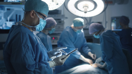 Doctor is using Tablet in Operation Room During Operation on Background.