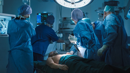Medical Team Performing Defibrillation in Modern Operating Room. Everyone is looking on Cardiac Monitor. - obrazy, fototapety, plakaty