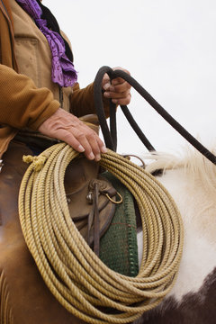 A ranch cowboy holds a coiled rope along his saddle