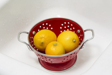 Lemons in a red colander in a white porcelain sink
