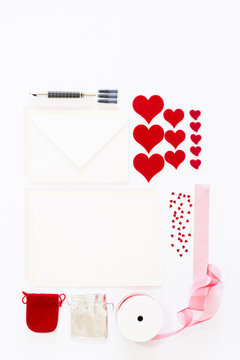 Display of love letter items on white background. Assortment of cards, envelopes, hearts, ribbon and ink pen.