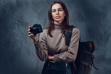 A woman with backpack holds compact photo camera.
