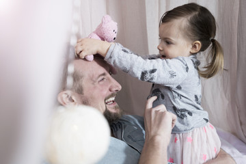 Happy father playing with toddler daughter in toy teepee