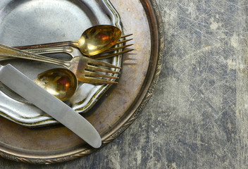 Overhead perspective of tarnished silver plated flat ware and platter with worn pewter dish on rustic steel background