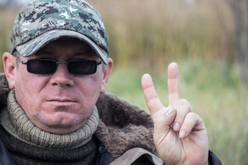 Portrait of a brutal man. The man in dark glasses, a warm sweater and a cap. He also shows his...