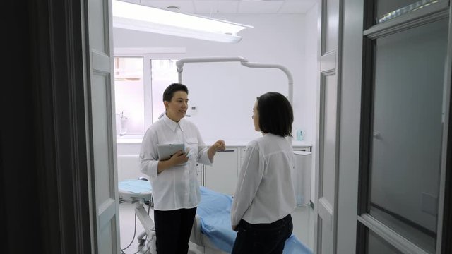 Dentist talking with young female patient in at the dentist clinic.