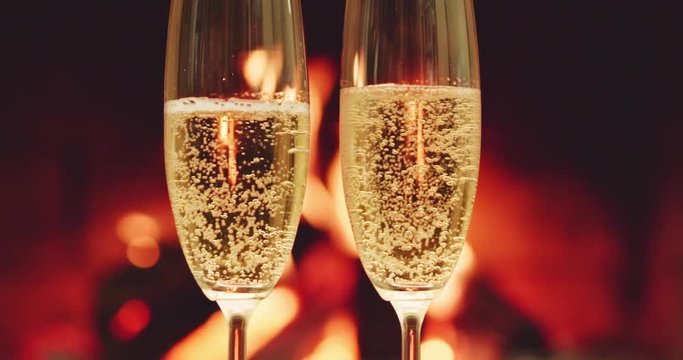 Sparkling champagne wine in glasses in front of the warm fireplace. Close up. Zoom out, Dolly shot. 4k graded from RAW. 
