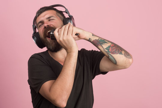 Dj with beard wears headphones. Man sings on pink background,