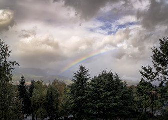 Obraz na płótnie Canvas Fantastical Atmospheric Mountainous Landscape with Central Rainbow in Stormy Cloudy Sky