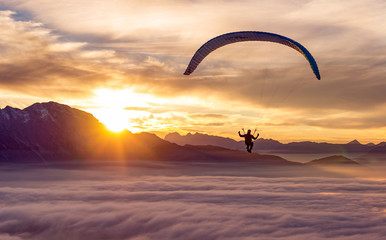 An adventurous sportsman does paragliding above the clouds at sunset.