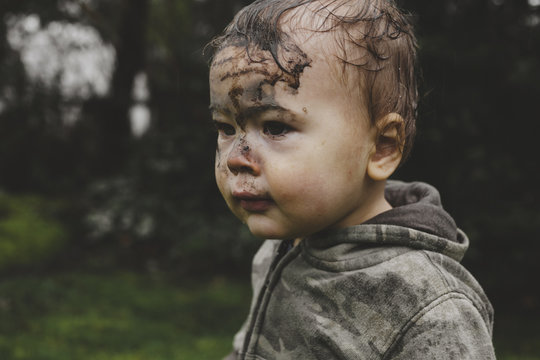 Cute young toddler boy outside in the rain with face covered in mud - funny
