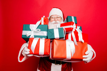 Festive seosonal occasion. Holly jolly x mas! Funny excited friendly generous santa`s face is popping up of gifts, he is presenting, red traditional fur coat, isolated on red background