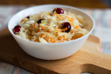 Sauerkraut with carrots and cranberries in a white bowl on the background of a wooden board. Marinated cabbage.