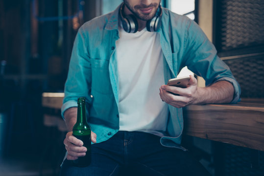 Chilling, technology, enjoying free time. Good life alone. Close up cropped of bearded music lover with bottle at the bar, sitting in casual smart, trendy and fashionable, watching at his telephone