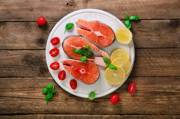 Salmon steaks with lemon, herbs, spices cherry tomatoes on wooden background. Healthy diet food concept. Top view. Copy space