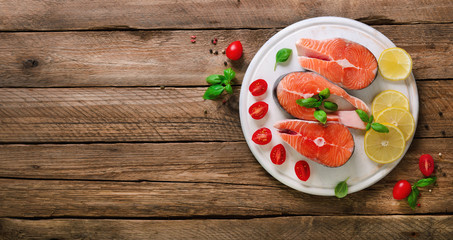 Salmon steaks with lemon, herbs, spices cherry tomatoes on wooden background. Healthy diet food concept. Top view. Copy space