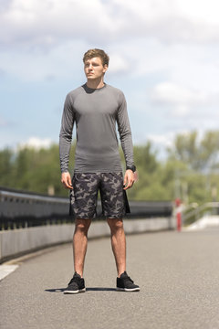 Young man in sportswear standing outdoor in sunny day in the city looking right.