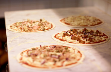 raw pizza with grated cheese on table at pizzeria