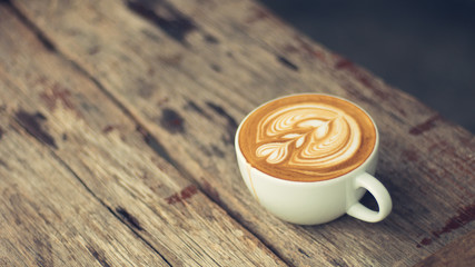 a cup of hot latte coffee on aged brown wood, heart shape latte art, coffee lover concept, vintage tone