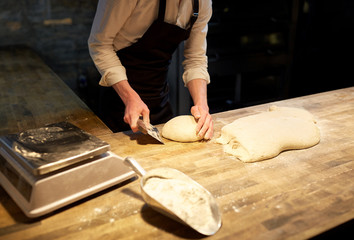 baker portioning dough with bench cutter at bakery