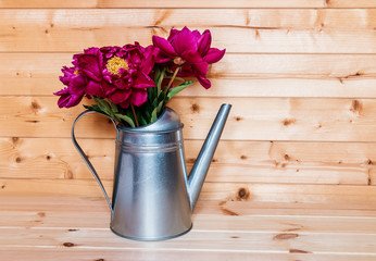 Bouquet of red peonies in watering can on wooden background
