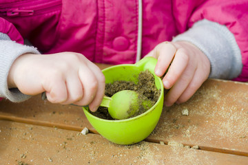 Dziecko bawi się piaskiem w kubeczku. Zdjęcie na dworze w piaskownicy.