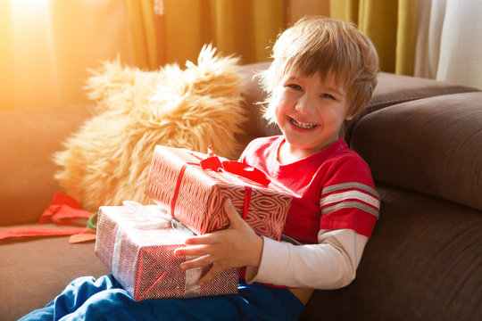 Happy child holding Christmas presents in the morning in the room. Christmas time.  Birthday..