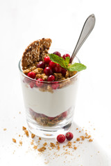 dessert with granola, cranberries and cream in glass on white table, closeup