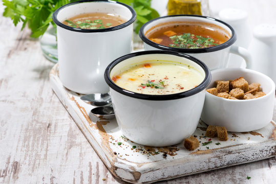 assortment of hot soups in mugs on wooden board
