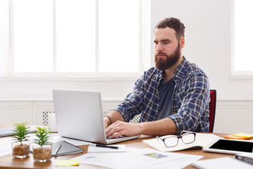 Young concentrated businessman with laptop in modern white office