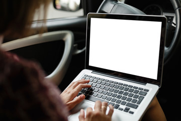 Crop mockup image of casual woman watching and using laptop while sitting on driver's seat in car.