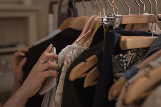 Cropped hand of woman with phone choosing clothes