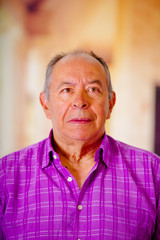 Portrait of a happy mature man wearing a purple square t-shirt in a blurred background