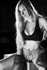 Fototapeta premium Half portrait of young blonde woman with long hair, dressed in black sports bra, pink shorts and red boxing gloves, looking to right side. Lovely female boxer posing. Concept of strength and power.