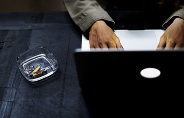 Hands using a laptop featuring a cigarette in an ashtray