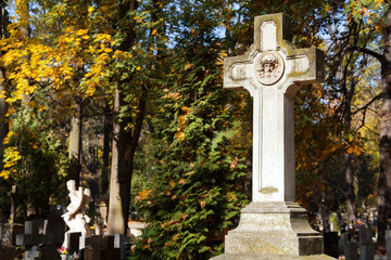 Old stone memorial cross at cemetery. Religious Christian symbol on autumn trees background