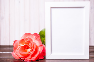 blank photo frame with copyspace and pink rose flowers on wooden background. greeting card .