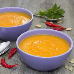 A bright cream soup of pumpkin on a gray wooden table.
