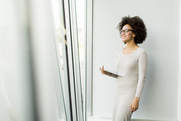 Young African American businesswoman standing wirth tablet in the office by window